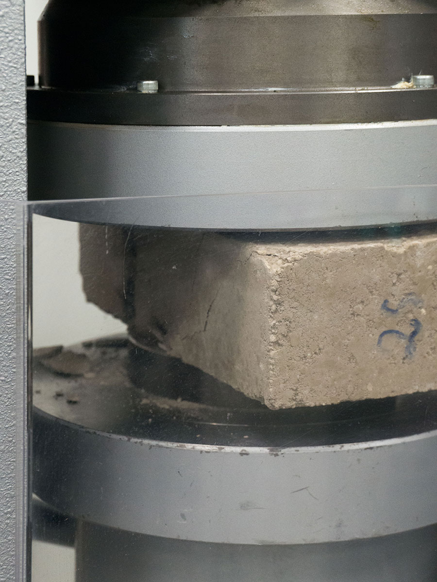 Photo of a Compressed Earth Block (CEB), being tested in a compression machine, assessing its structural integrity and load-bearing capacity.